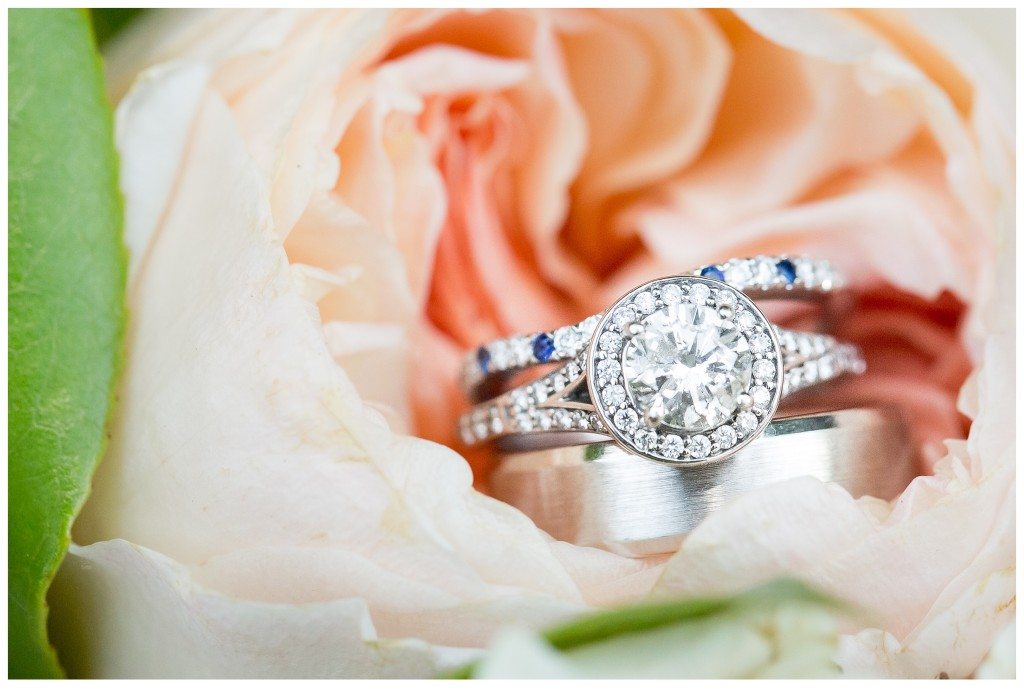 Bridal wedding ring set showing diamond rings and a platinum mens band posed in front of a peach flower. 