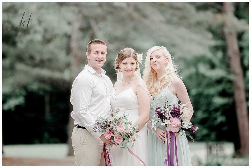 Bride, Groom and Bridesmaid wearing mint green wedding dress take a photo at Camp Takodah in Rindge NH