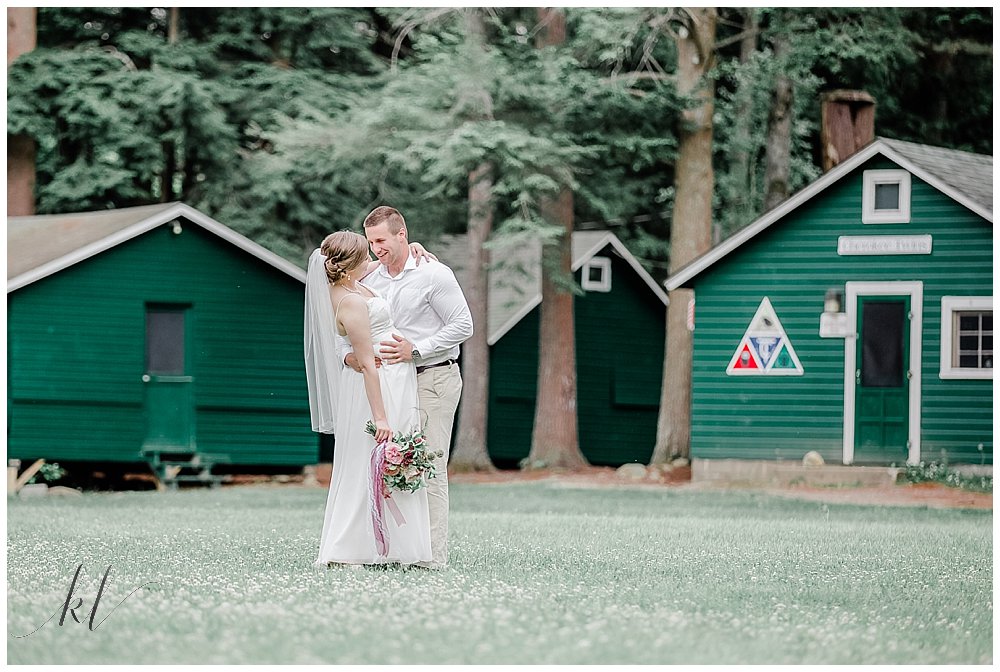 Natural and Authentic portrait of Bride and Groom in front of the green cabins at Camp Takodah in Rindge NH. 