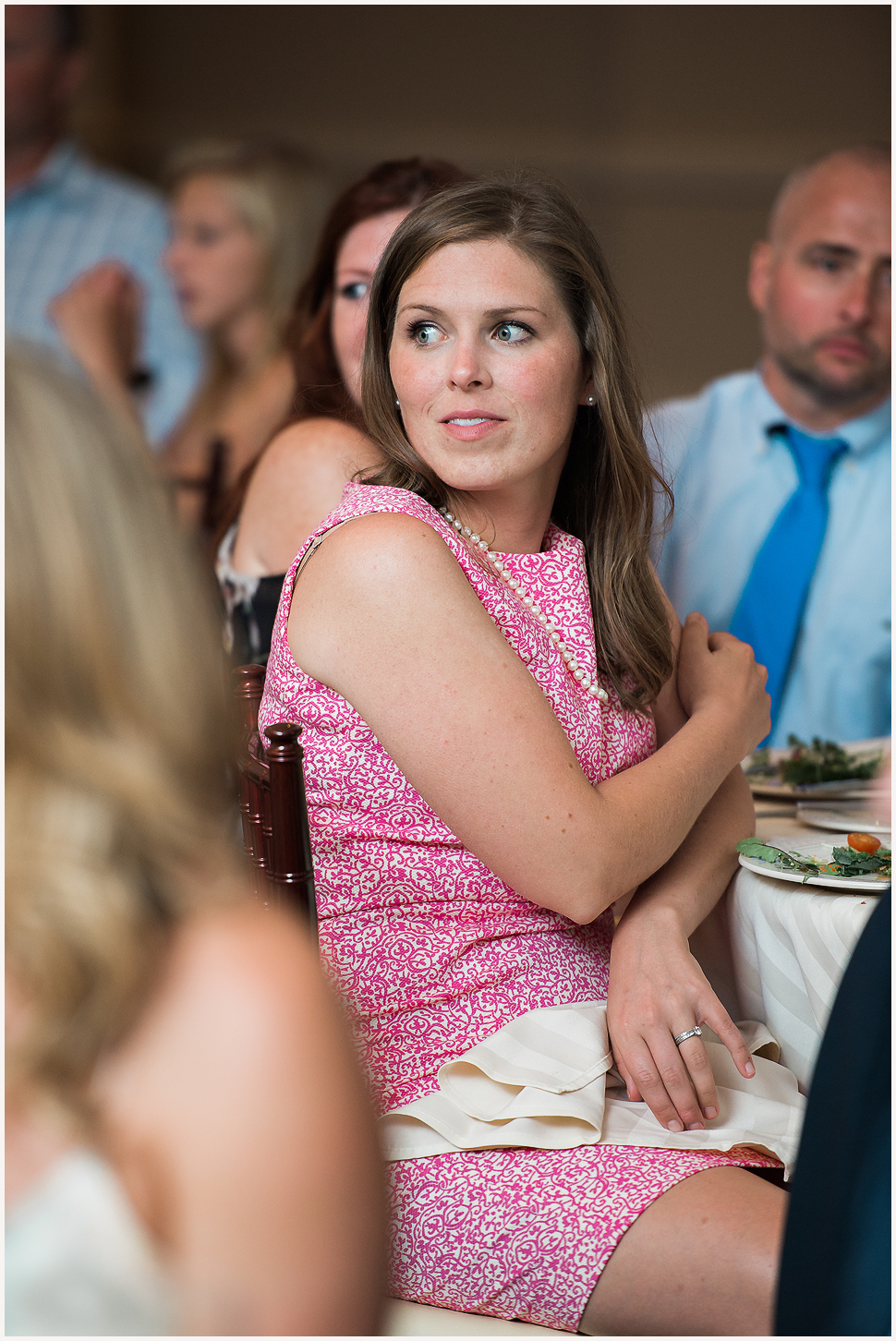 Candid photo of a girl in a pink patterned dress listening to a toast at a wedding reception. 