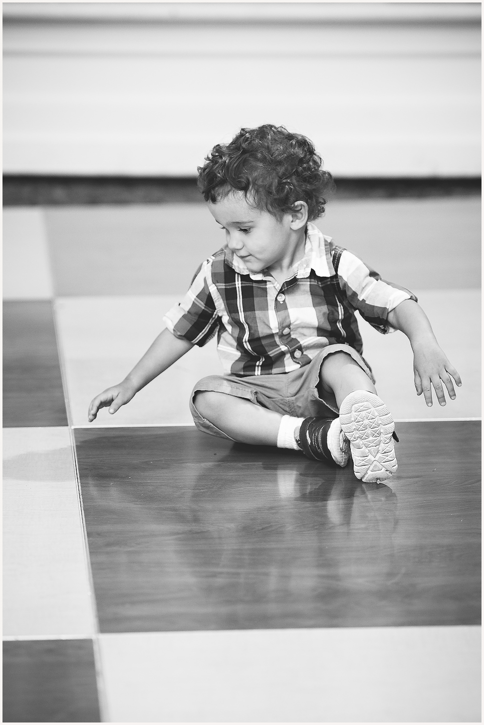 Candid black and white photo of a young boy sitting on a checkered floor. 
