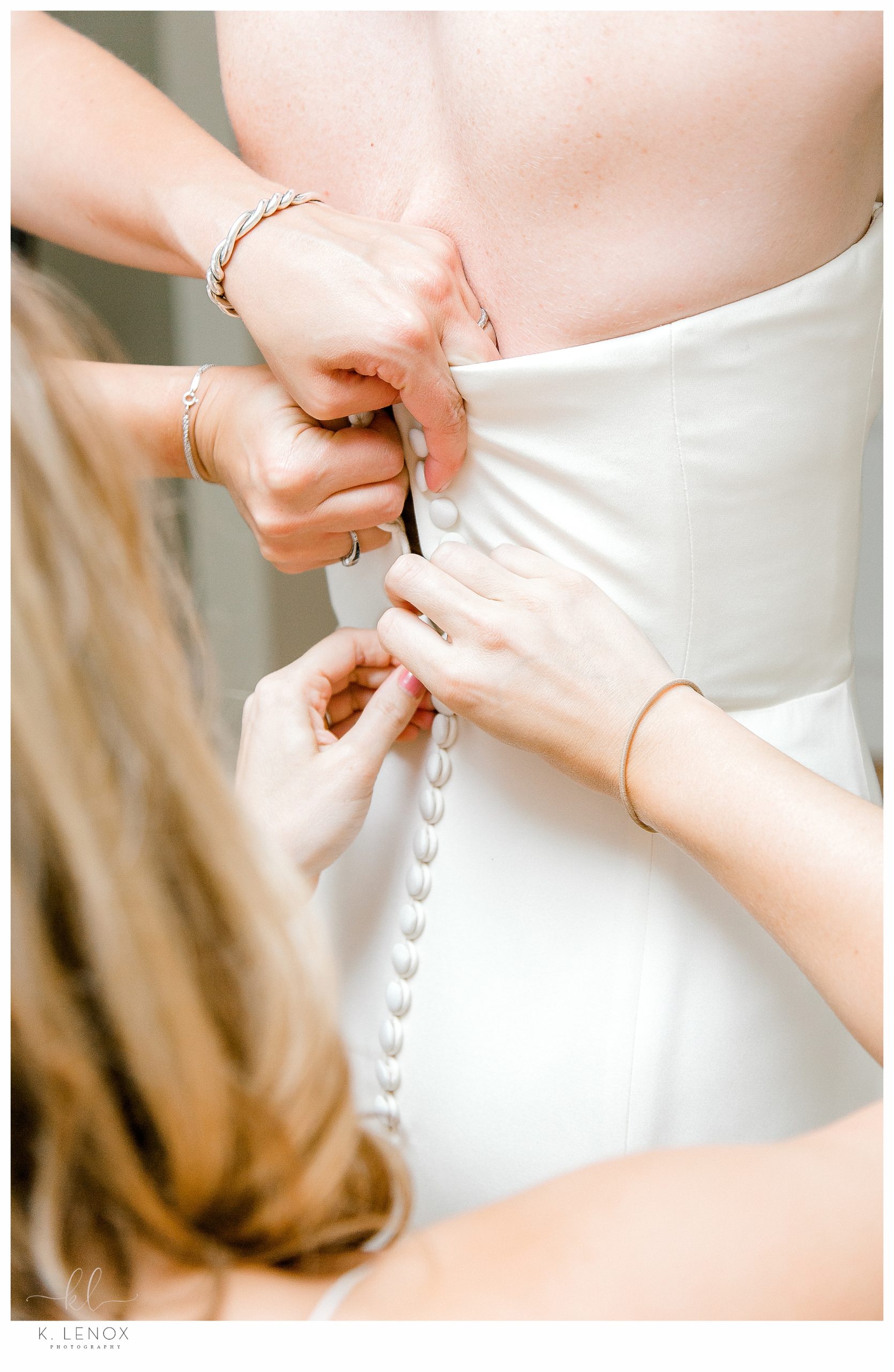 Closeup photo of a brides wedding dress getting buttoned. 