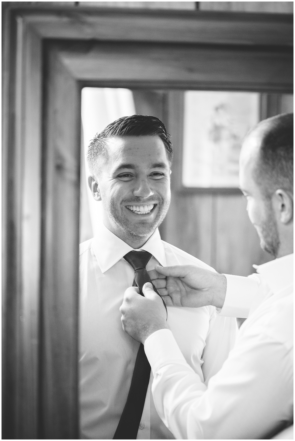 Black and White photo of a groom getting help with his tie. 