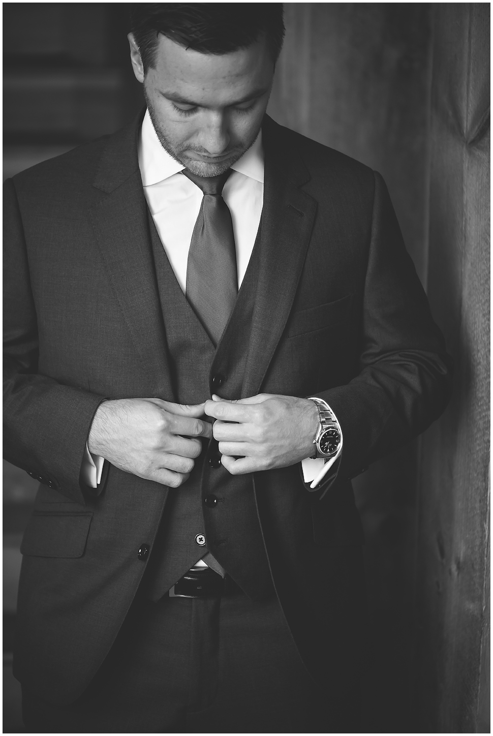 Black and white photo of a groom buttoning his vest on his wedding day at Alyson's Orchard. 