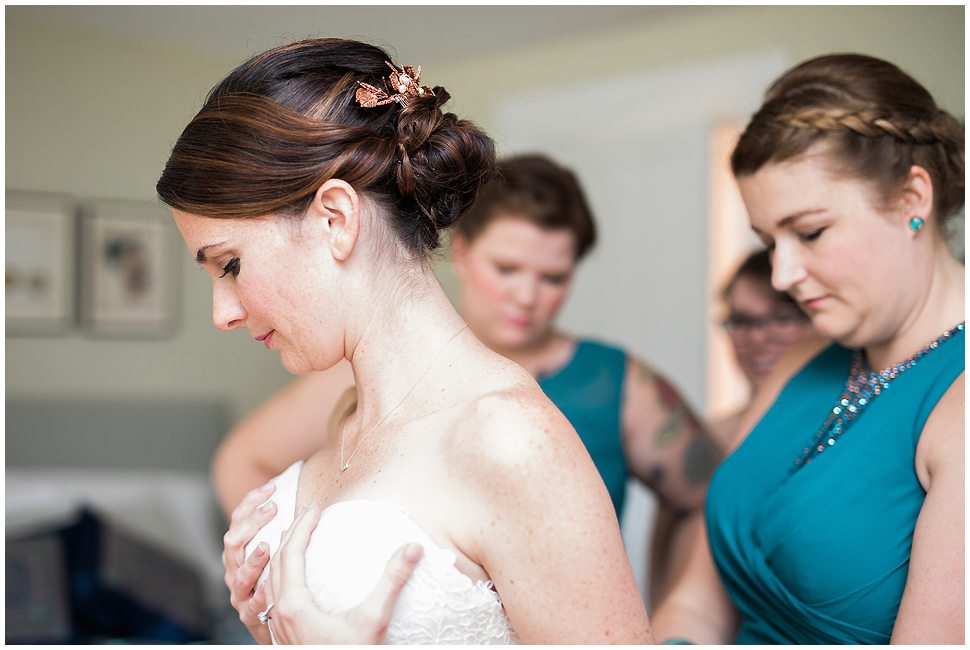 Photo of bridesmaids helping bride get into her wedding dress at Alyson's Orchards farm house. 