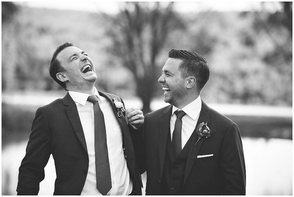 Candid Black and white photo of groom and best man laughing at Alyson's Orchard on his wedding day. 