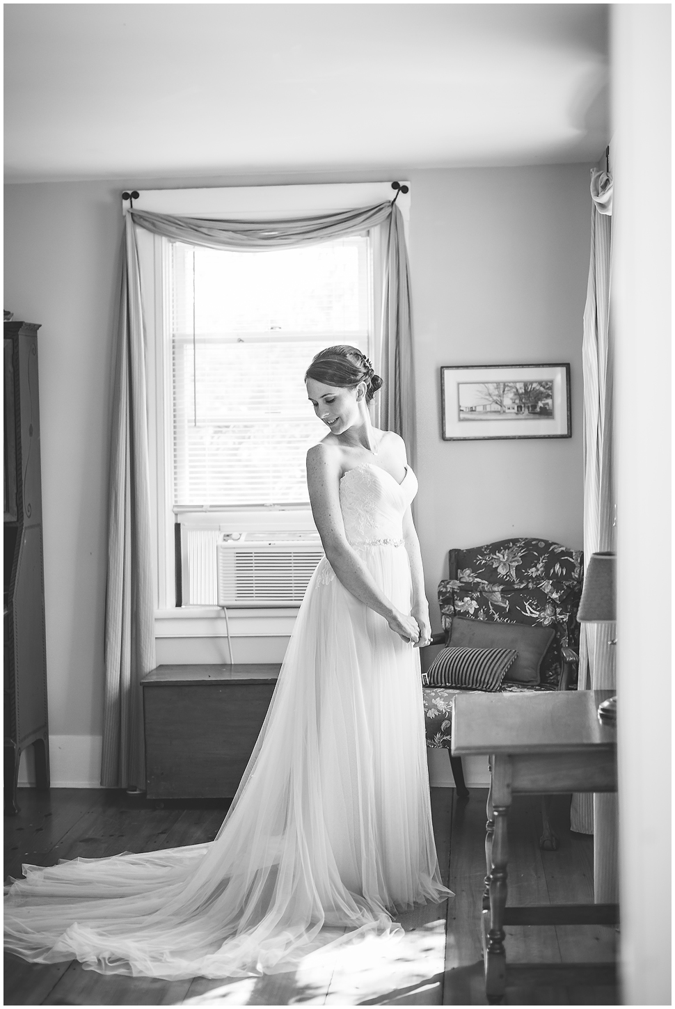 Black and White photo of a bride looking over her shoulder at her wedding dress train. 