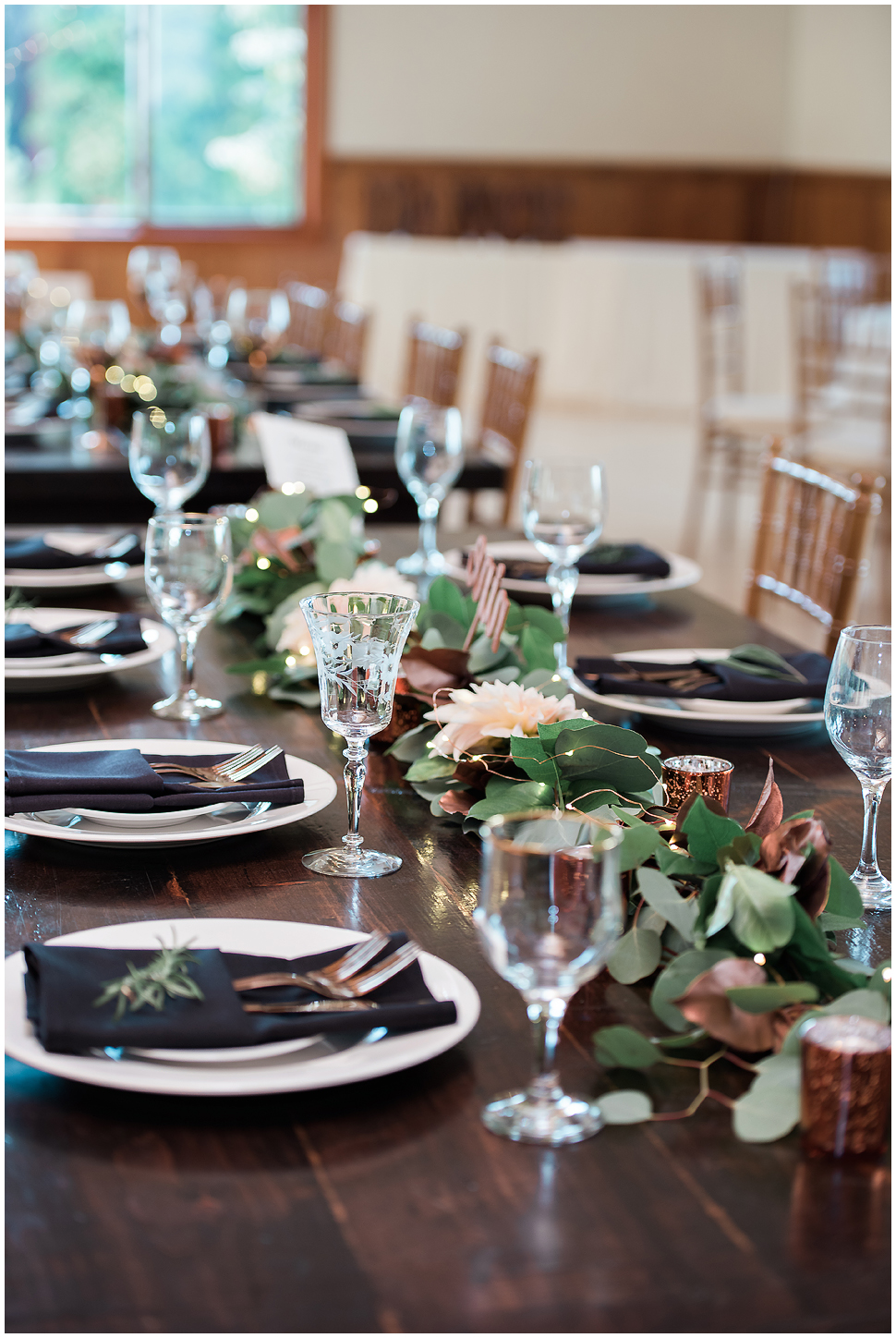 Farm table detail photo at wedding reception showing crystal water glass. eucalyptus garland
