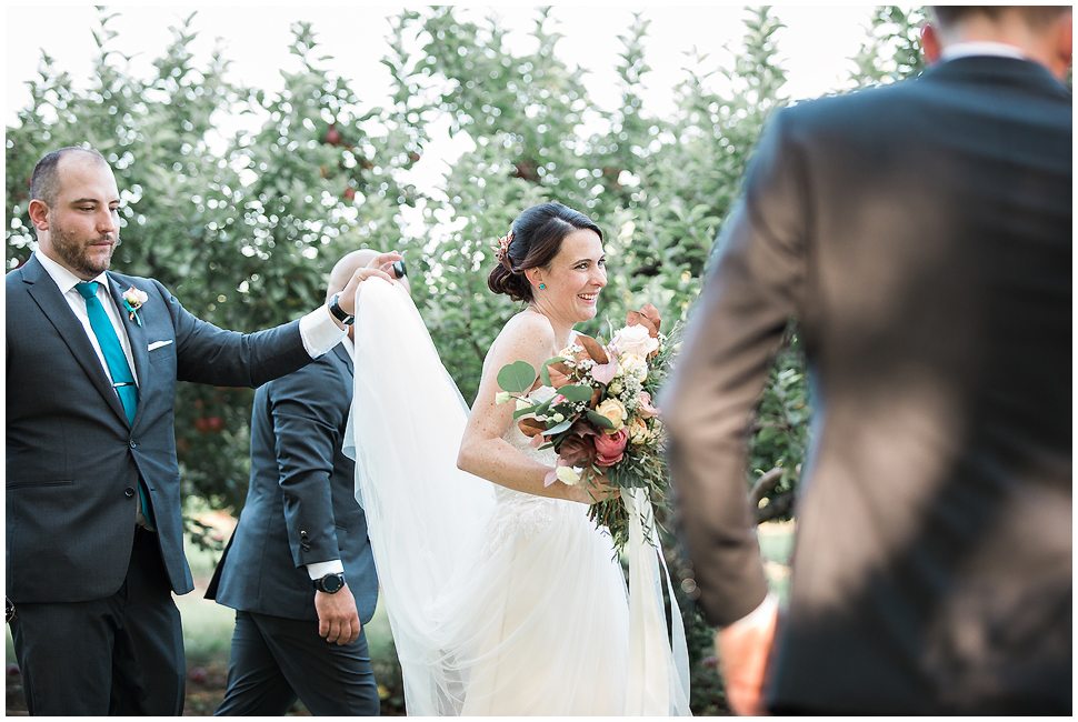 Candid photo of a groomsman helping bride hold her dress as she walks. 