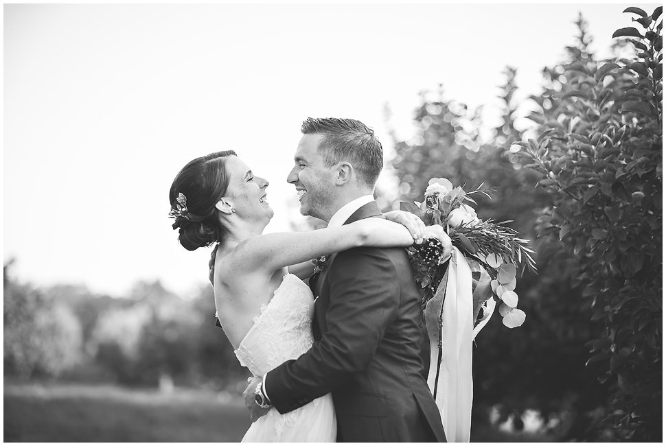 Black and white photo of a bride and groom hugging and laughing. 