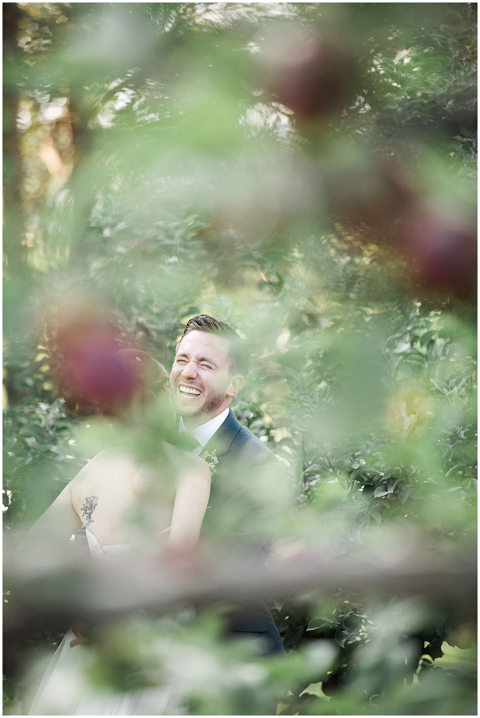 Creative portrait of a groom laughing on his wedding day with his wife in an orchard at Alyson's 