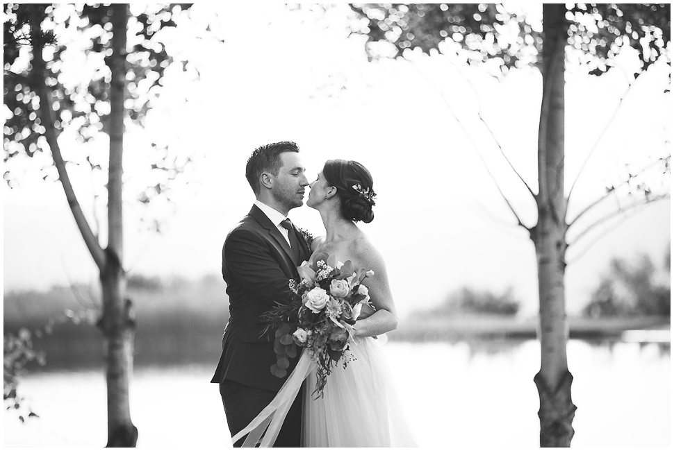 Black and White photo of a bride and groom kissing between two trees. 
