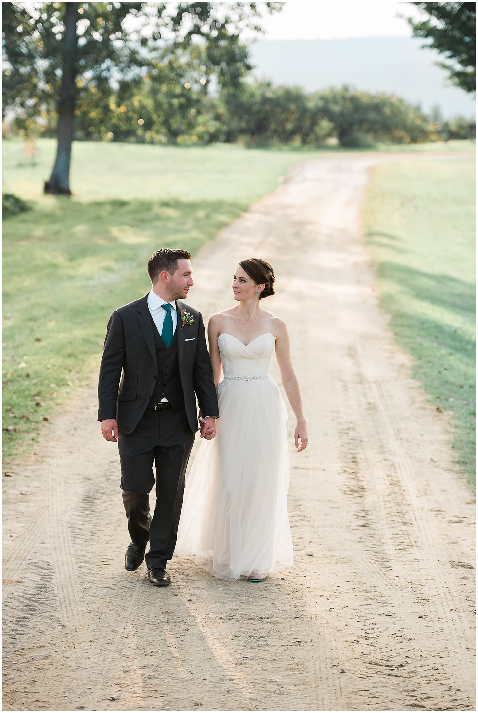 Bride and Groom walk hand in hand on a dirt path. 