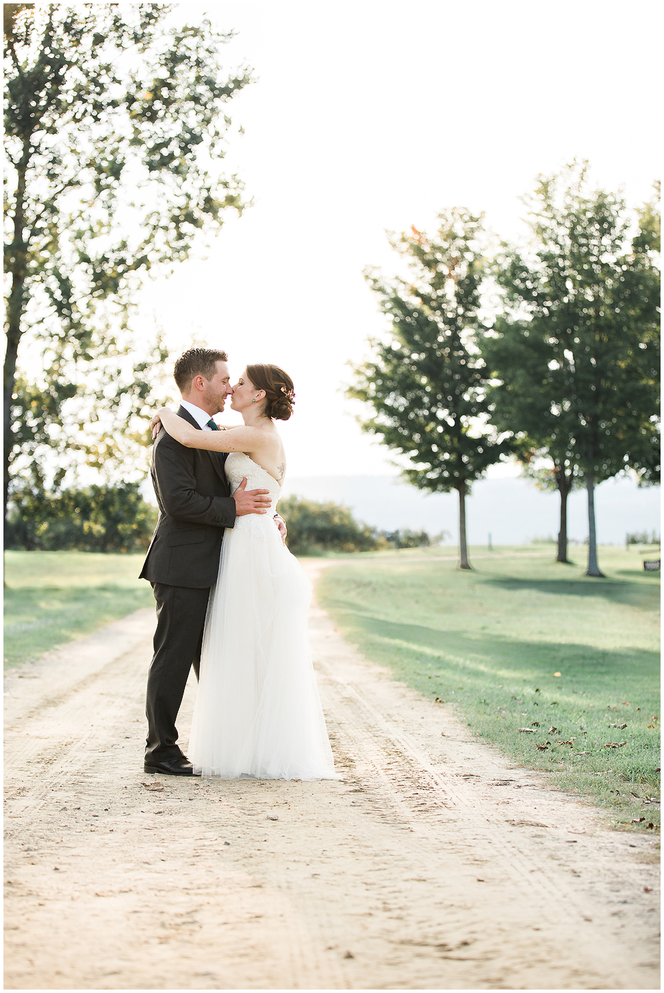 Bride and Groom hug and kiss on a dirt path on their wedding day. 