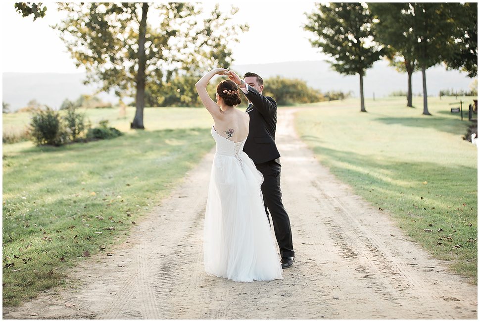 Bride and groom spin and dance outside on a dirt road on their wedding day. 