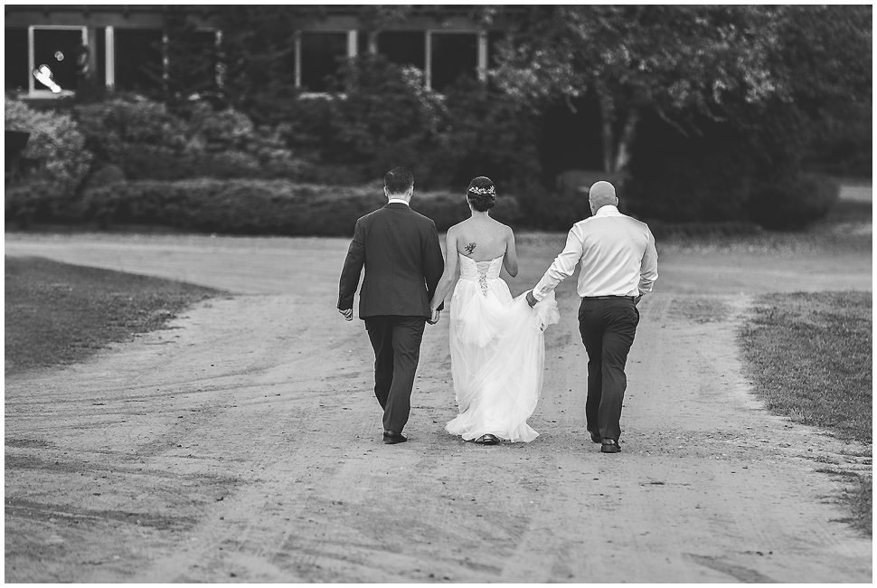 Bride and groom with groomsman walking back to wedding reception at Alyson's orchard. 