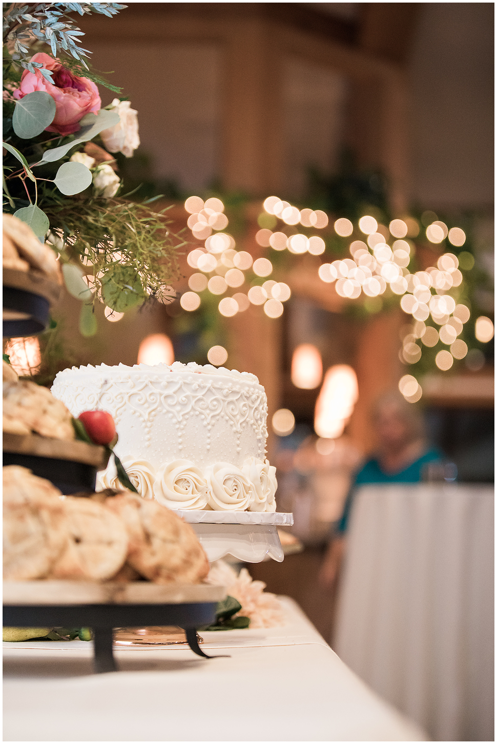 White frosted wedding cake with twinkle lights in the background. 
