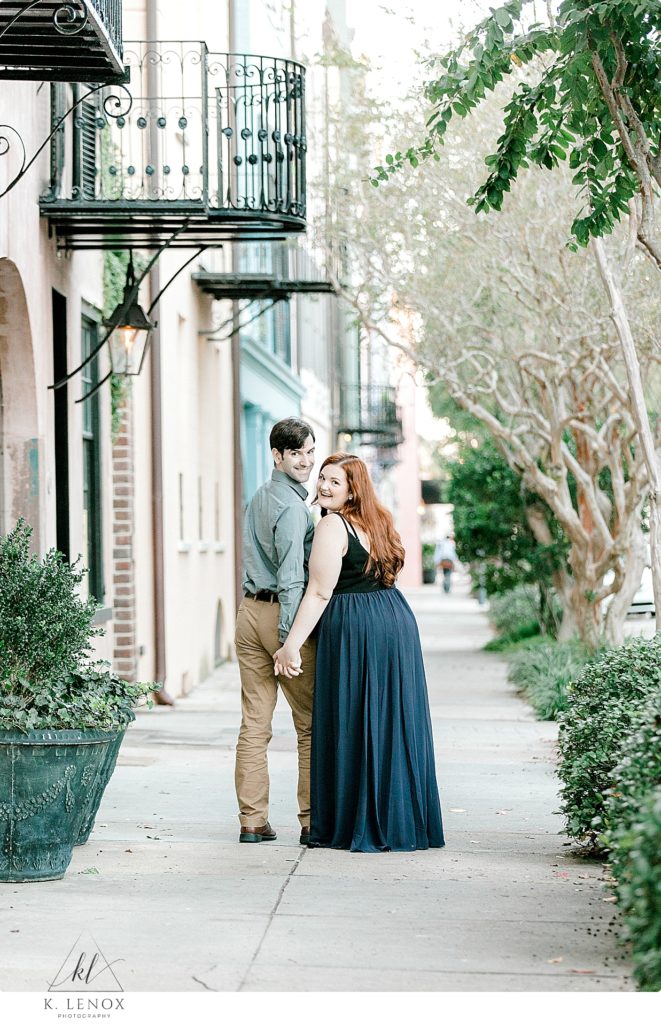 Man and Woman walking hand in hand down Rainbow Row in Charleston SC for their light and airy engagement session