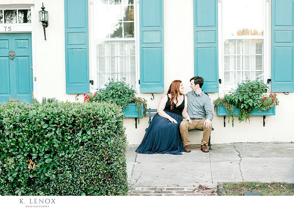Charleston SC Engagement Session- man and woman sitting on a bench with blue shutters behind them.  Rainbow Row Charleston SC
