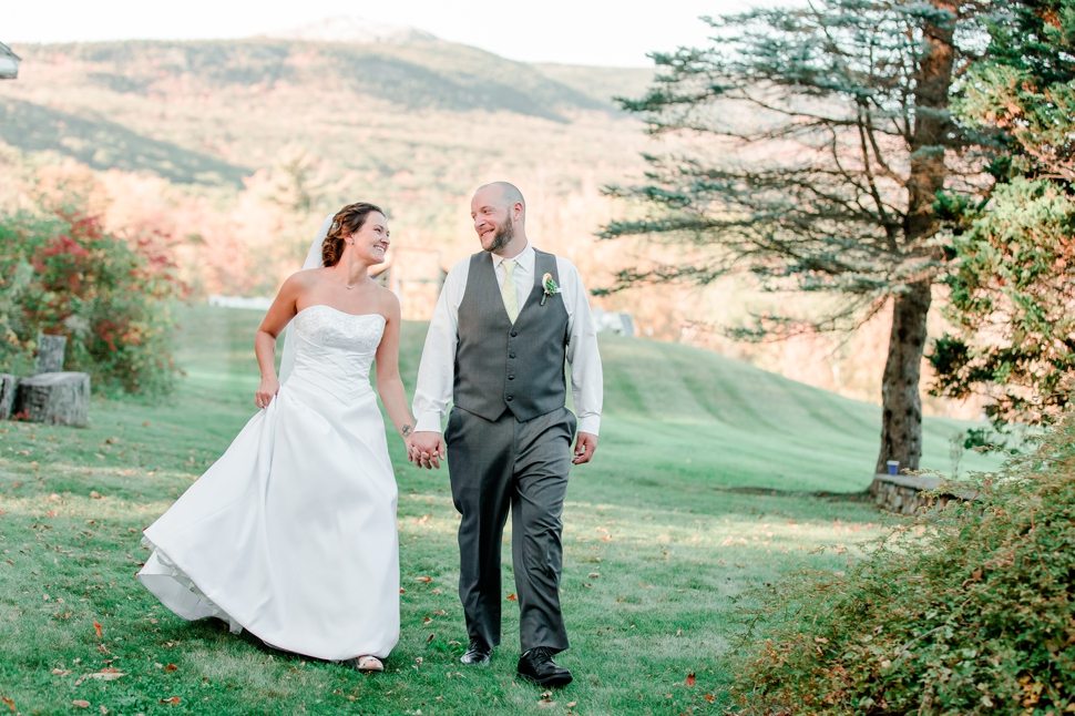 bride and groom walk hand in hand for a natural, unposed portrait in front of mount modnadnock in fall