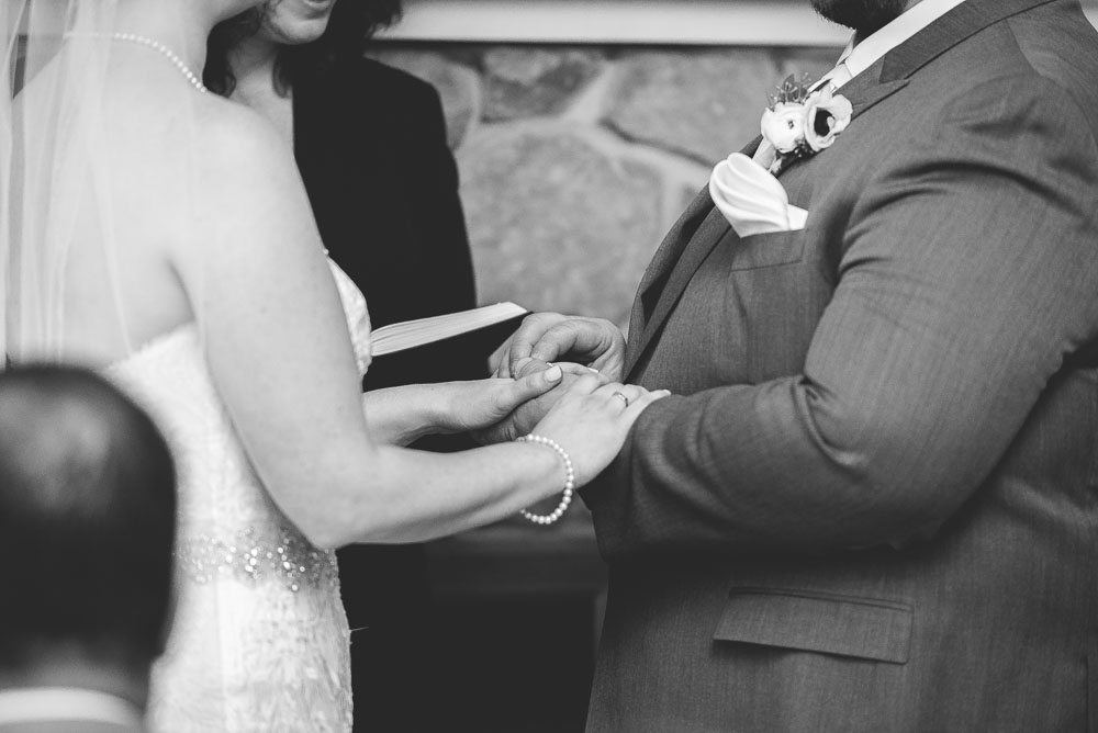 Photo is black and white close up of bride and grooms hands during the wedding ceremony. 