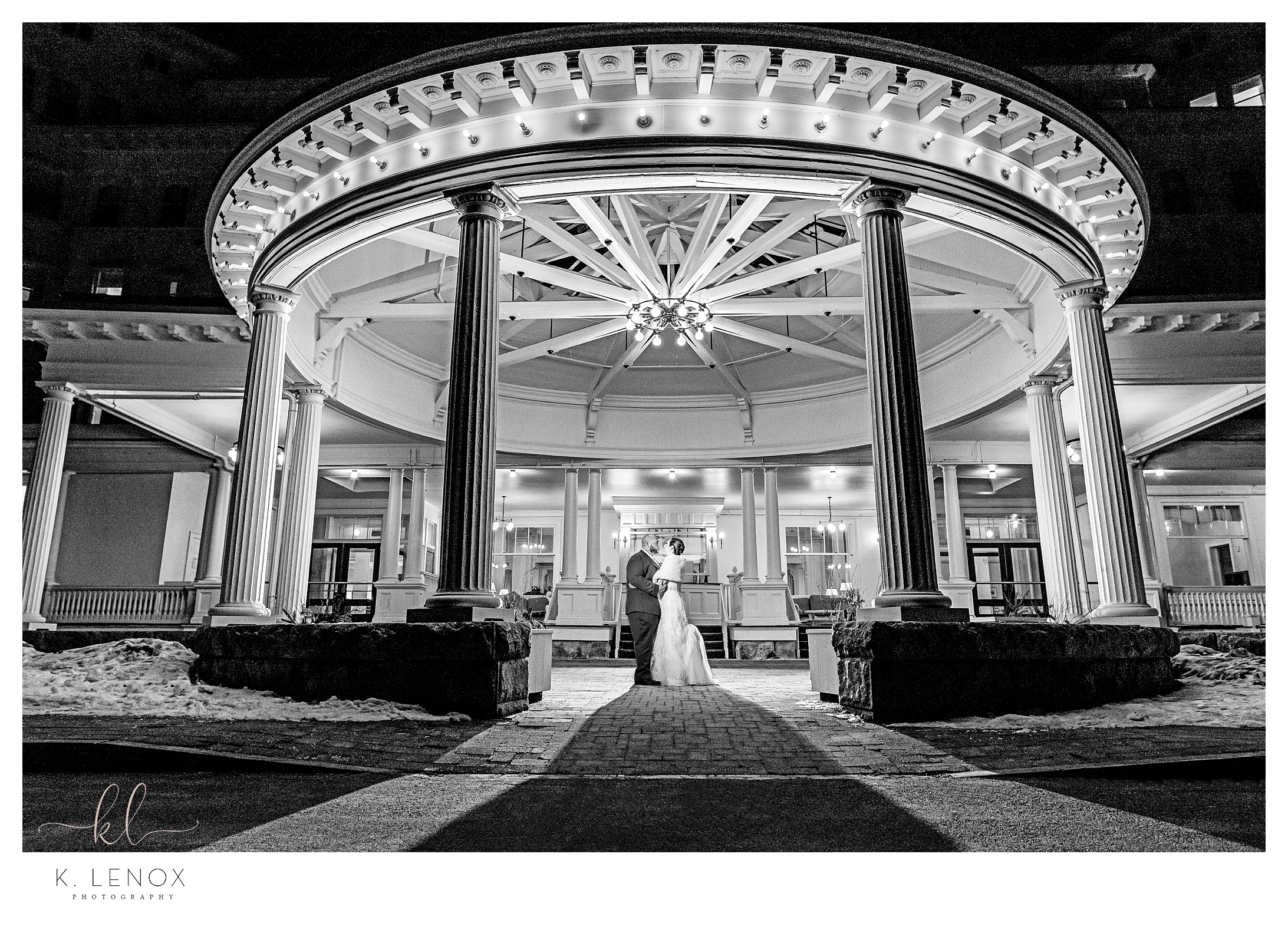 Black and white photo with a bride and groom in front of the Omni Mount Washington Resort at night. 
