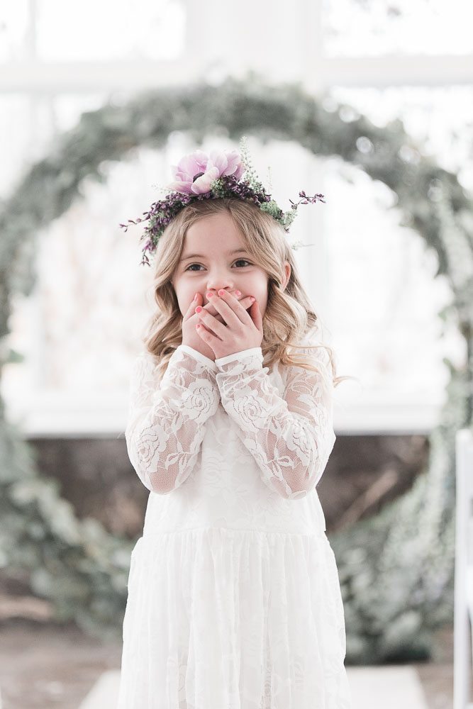 Young flower girl wearing a flower crown made of purple flowers and greenery. 