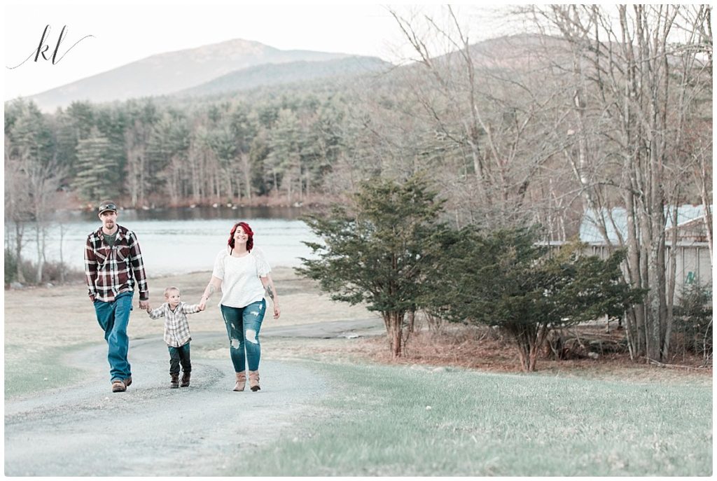 Fun Family Photo showing a family of three holding hands walking a path. In the back ground is Mount Monadnock. 