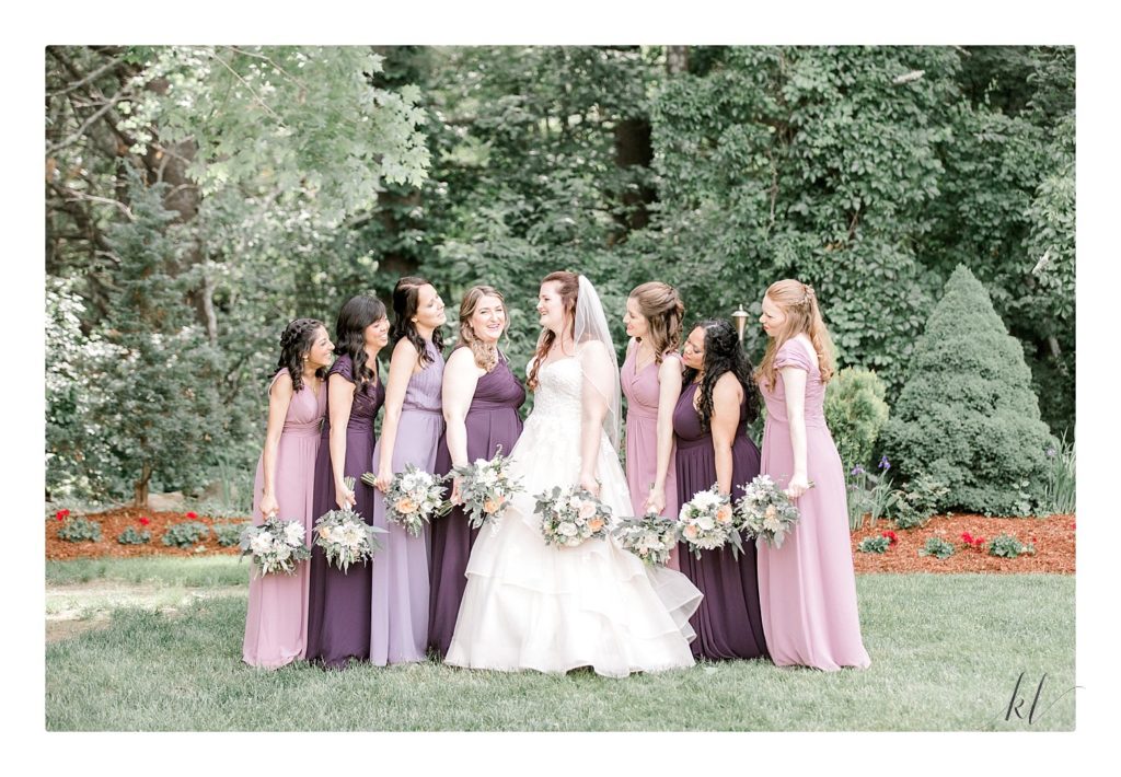 Elegant Bride in a Essense of Australia wedding gown with her 7 bridesmaids wearing different shades of purple dresses at the Bedford Village Inn 