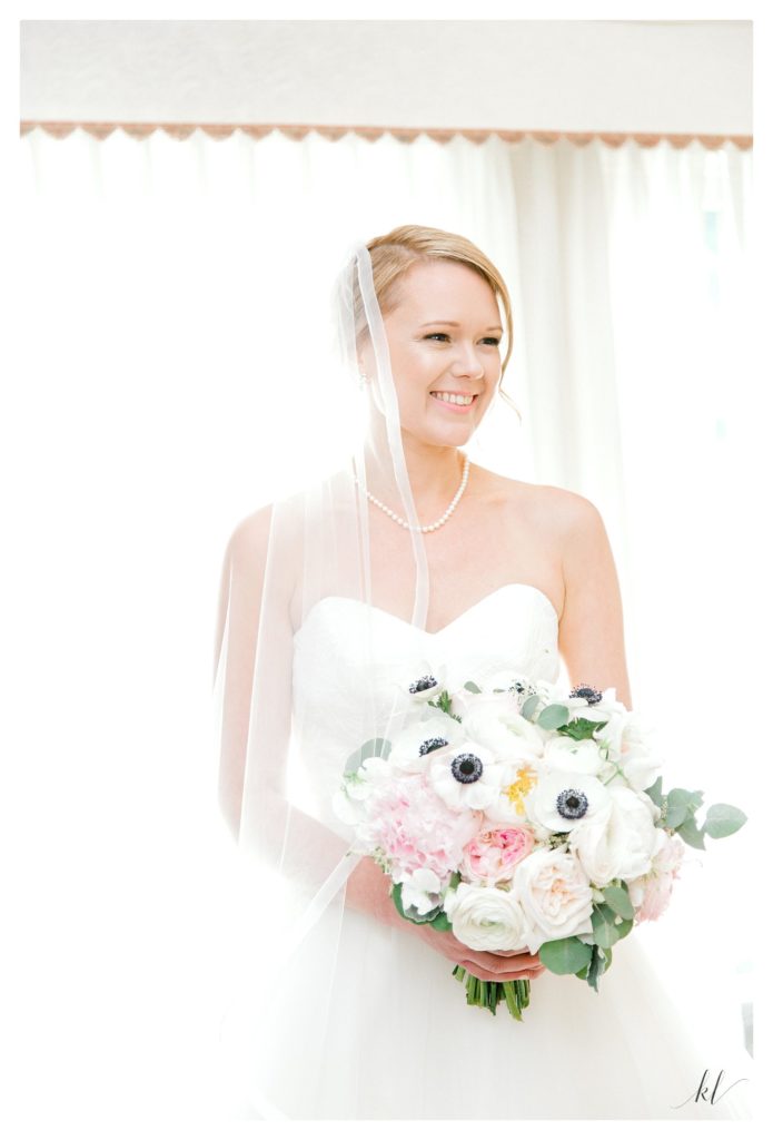 Bright and airy bridal portrait of girl holding her white anemone bouquet and wearing a blush by hayley paige gown. 