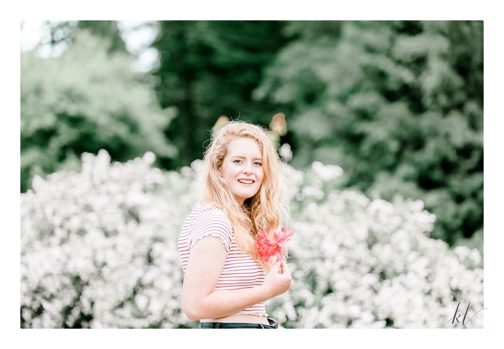 Beautiful Senior portrait of a blonde haired girl holding a pink flower.  Edited light and airy. 