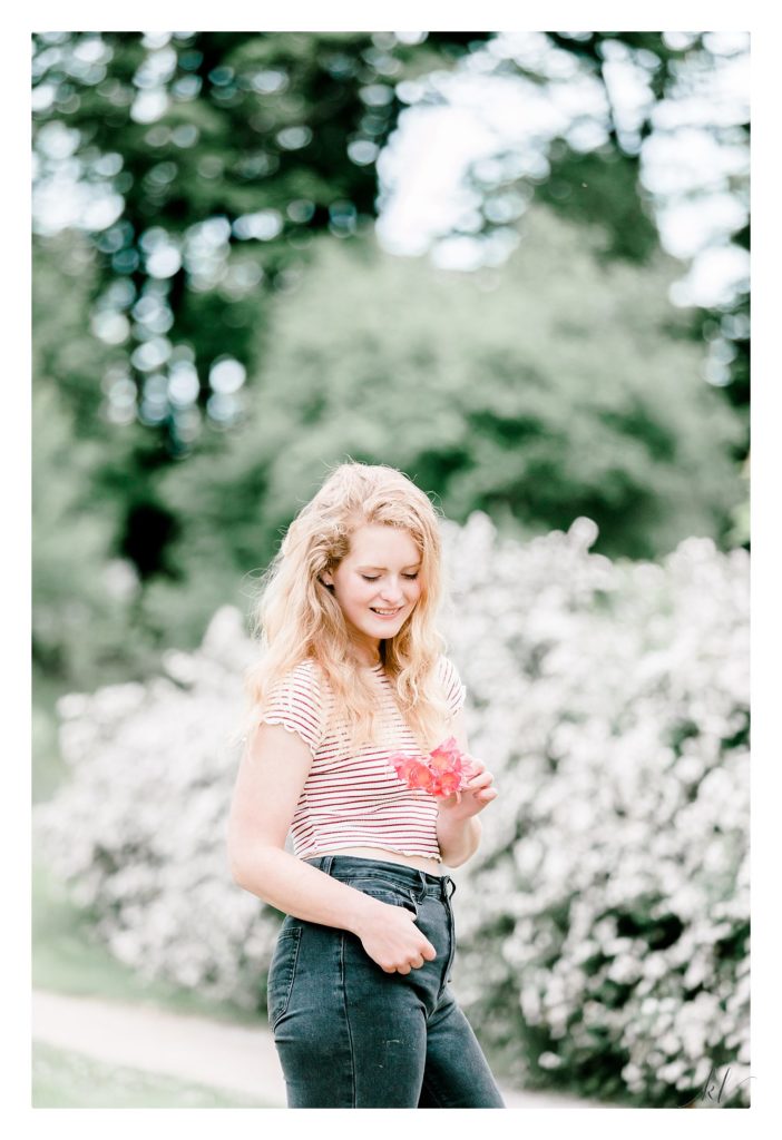 Light and Airy Keene Senior portrait of a pretty girl holding a red flower and wearing black jeans and a striped shirt.  Taken in Keene NH. 