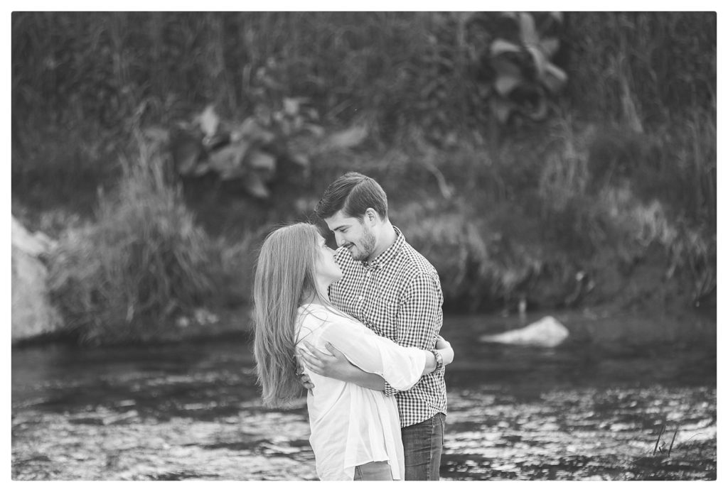 Black and White engagement photo of a man and woman on the side of a creek in the White mountains Region of NH. 