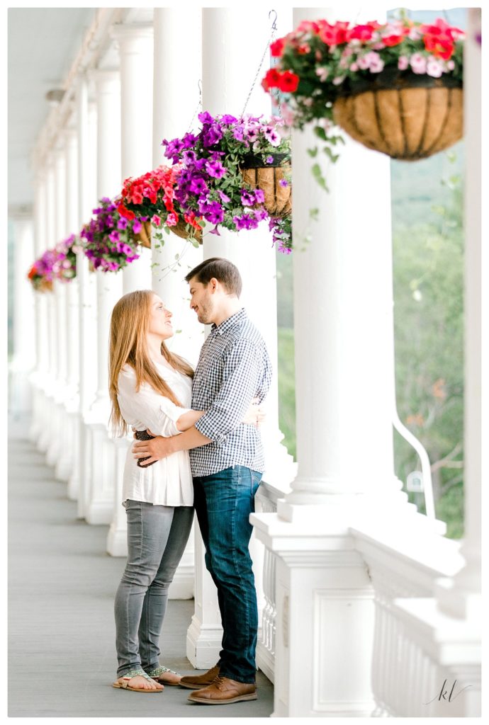 Man and woman standing on a porch with hanging flower baskets. 