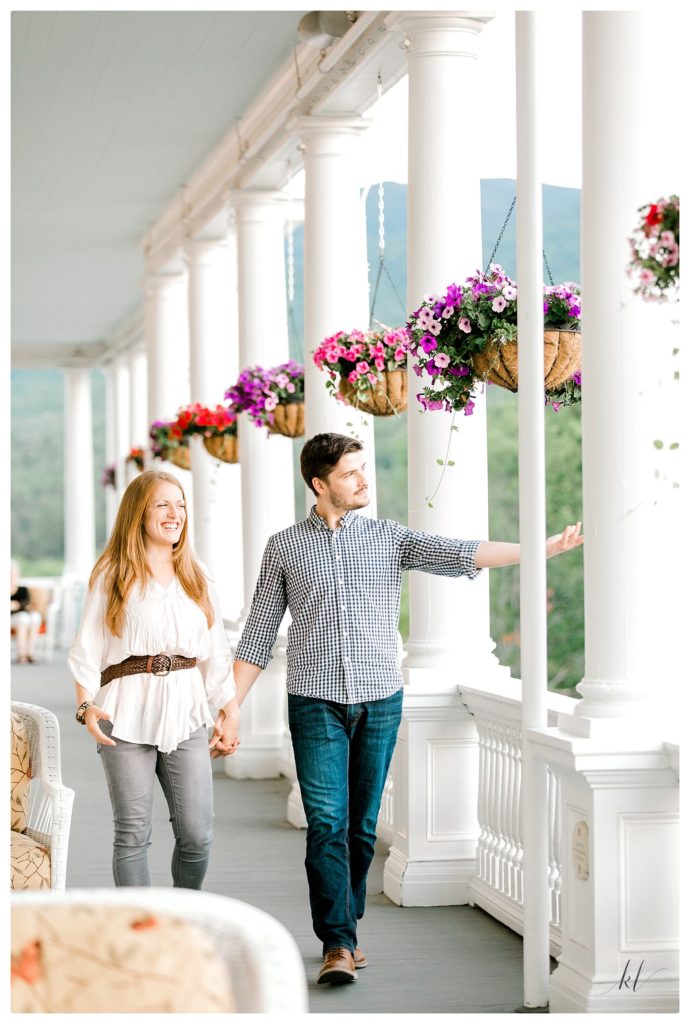 Man and woman walking on the porch of the Omni Mount Washington resort during their engagement session. 
