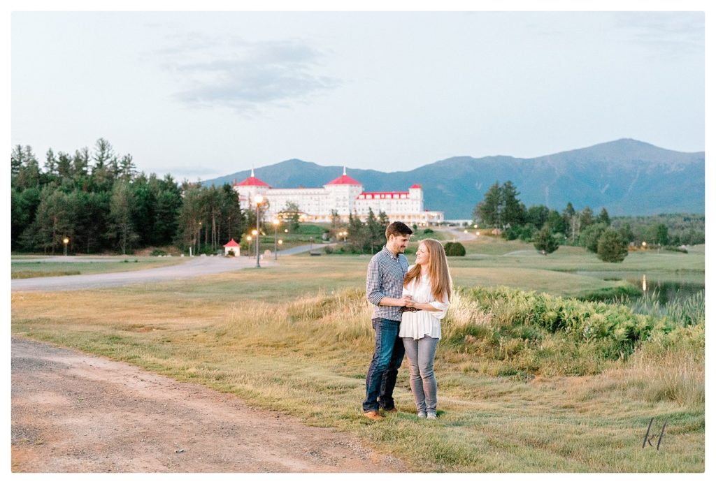 Man and woman posing in front of the Omni Mount Washington Resort during their Engagement Session at twighlight. 