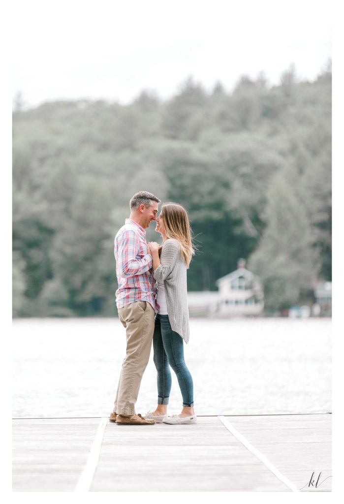 Rustic Engagement Photos of a man and woman standing hand in hand on a dock in Swanzey Lake. NH
