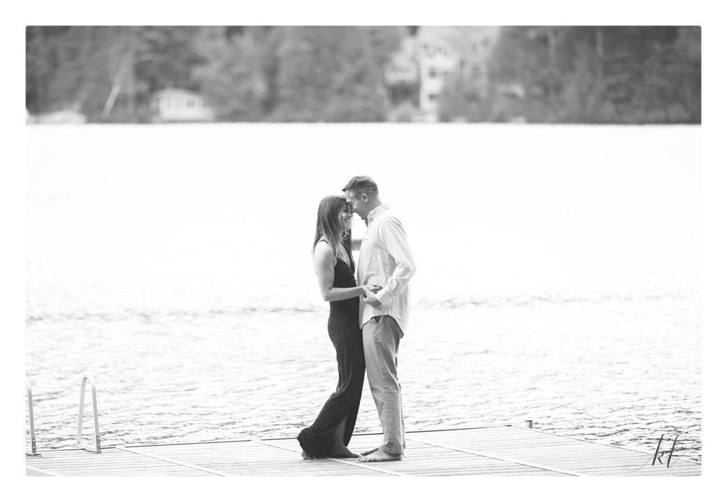 Black and White photo of an engaged couple on a dock in Swanzey Lake NH during their Rustic Engagement Session. 