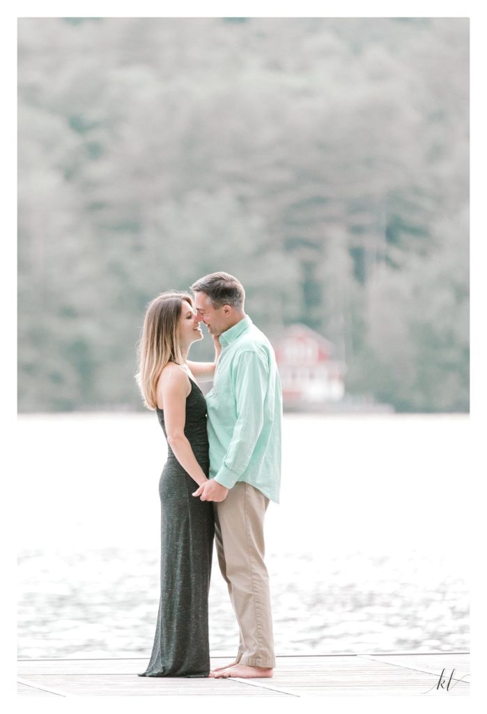 Man and Woman kissing on a dock during their Rustic Engagement Session on Swanzey Lake. 