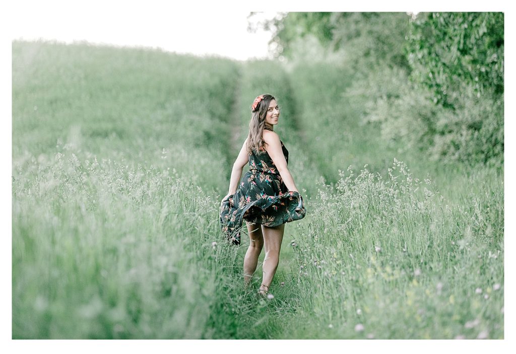 Boho inspired photo shoot showing a girl in a black flowered dress running in a field of green grass. 