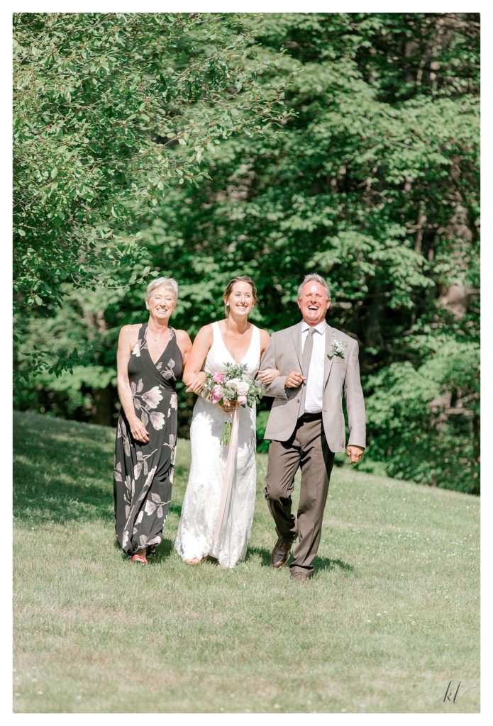 Candid photo of a bride walking down the aisle with her mom and dad during the full on heat of the day. 
