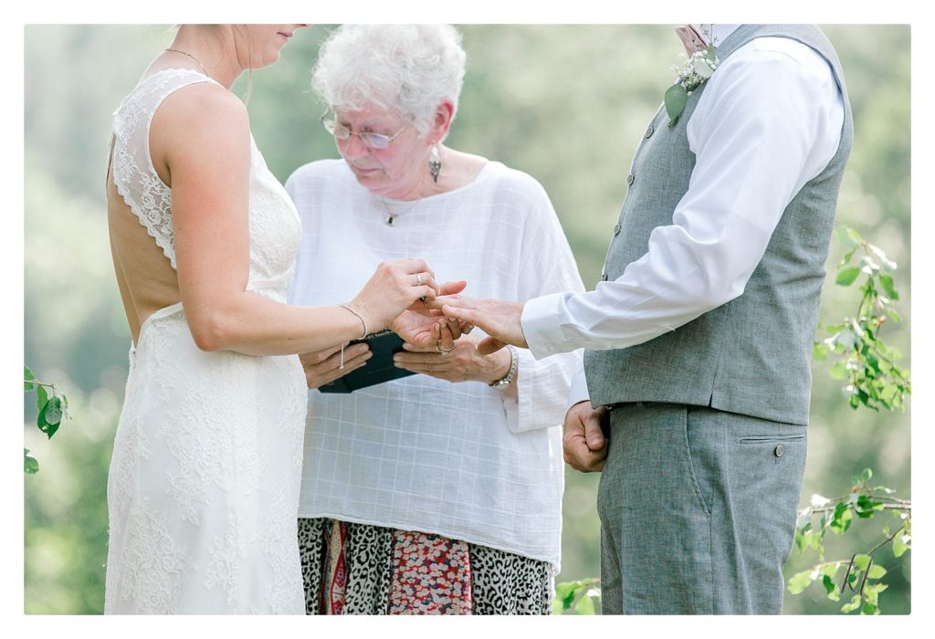 Bride puts on her groom's wedding band during their Casually Elegant Backyard wedding ceremony. 