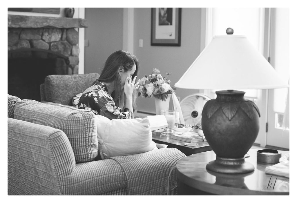 Black and white photo of a bride wiping a tear away after reading the card from her groom on their wedding day. 