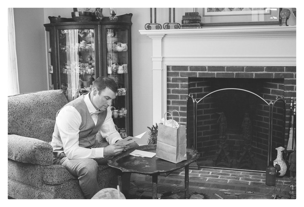 black and white photo of a groom opening the gift from his bride on their wedding day. 