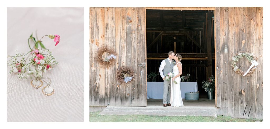 Bride and groom kiss in front of the rustic barn with wreathes on the doors. 