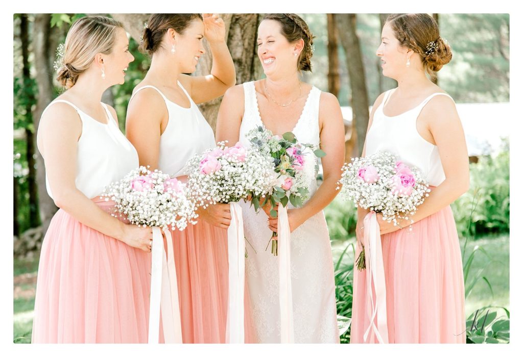 Light and airy candid photo taken of a bride and her three bridesmaids wearing pink skirts and baby's breath bouquets