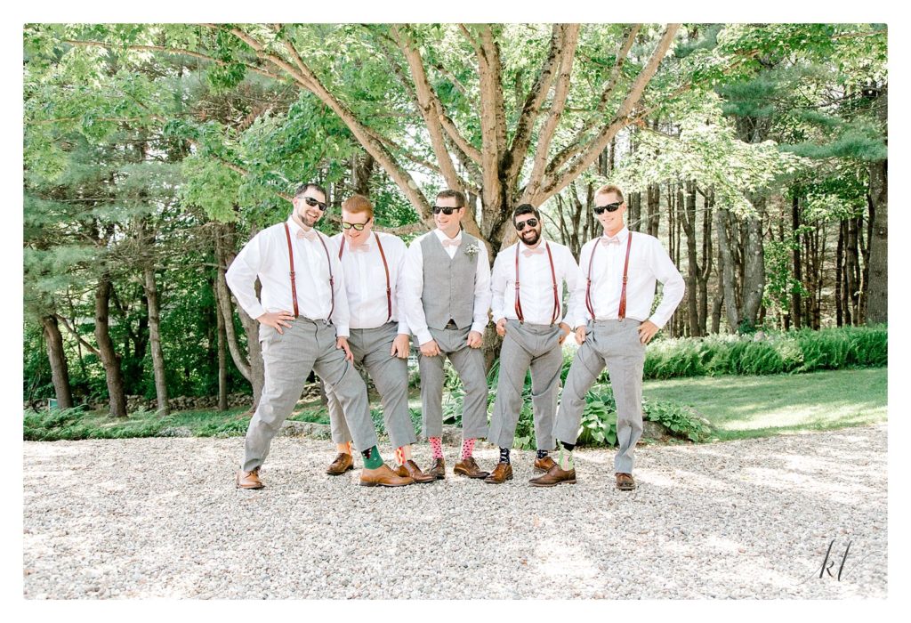Groom and four groomsmen pose showing their fun socks and wearing sunglasses for his casually elegant backyard wedding. 