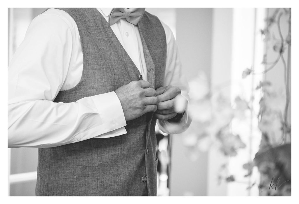Black and white photo of the groom buttoning his vest for his casually elegant backyard wedding