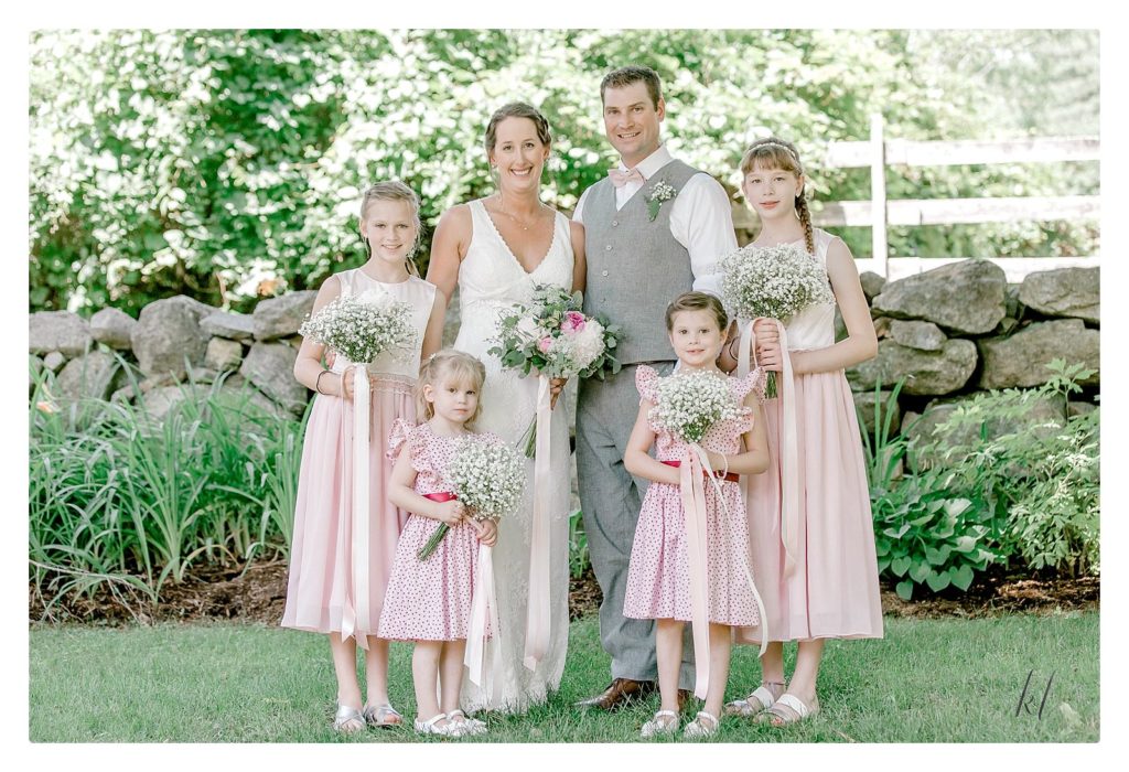 Formal portrait of the Bride and groom with the Jr. Bridesmaids and flower girls wearing pink and holding baby's breath