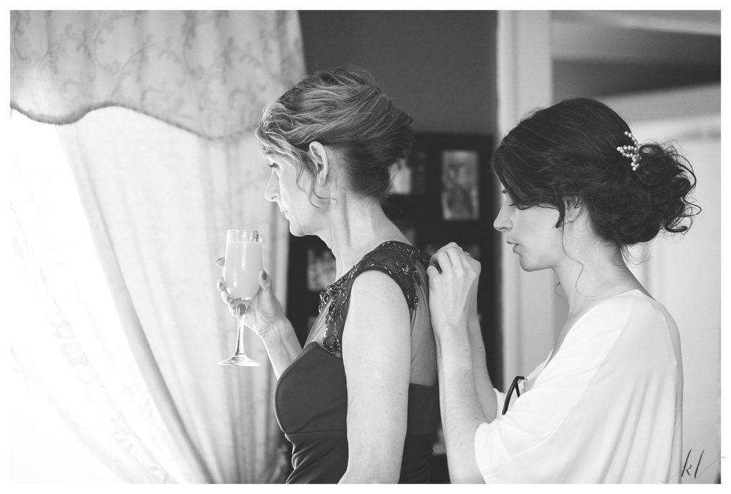 Black and White image of a bride buttoning her mother's dress on her wedding day. 